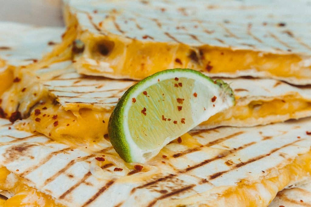 Grüne Limette liegt auf drei saftigen Käse Quesadillas